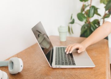 Escritorio con un portátil y una mano sobre las teclas, representando el uso de herramientas digitales para el control horario y la gestión eficiente de la jornada laboral.